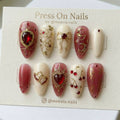 Almond-shaped press on nails with red heart gems, gold celestial moons, and cherry motifs on ivory and jelly red bases.