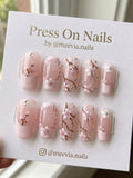 Square-shaped pink press-on nails with cherry blossom floral art and small rhinestones