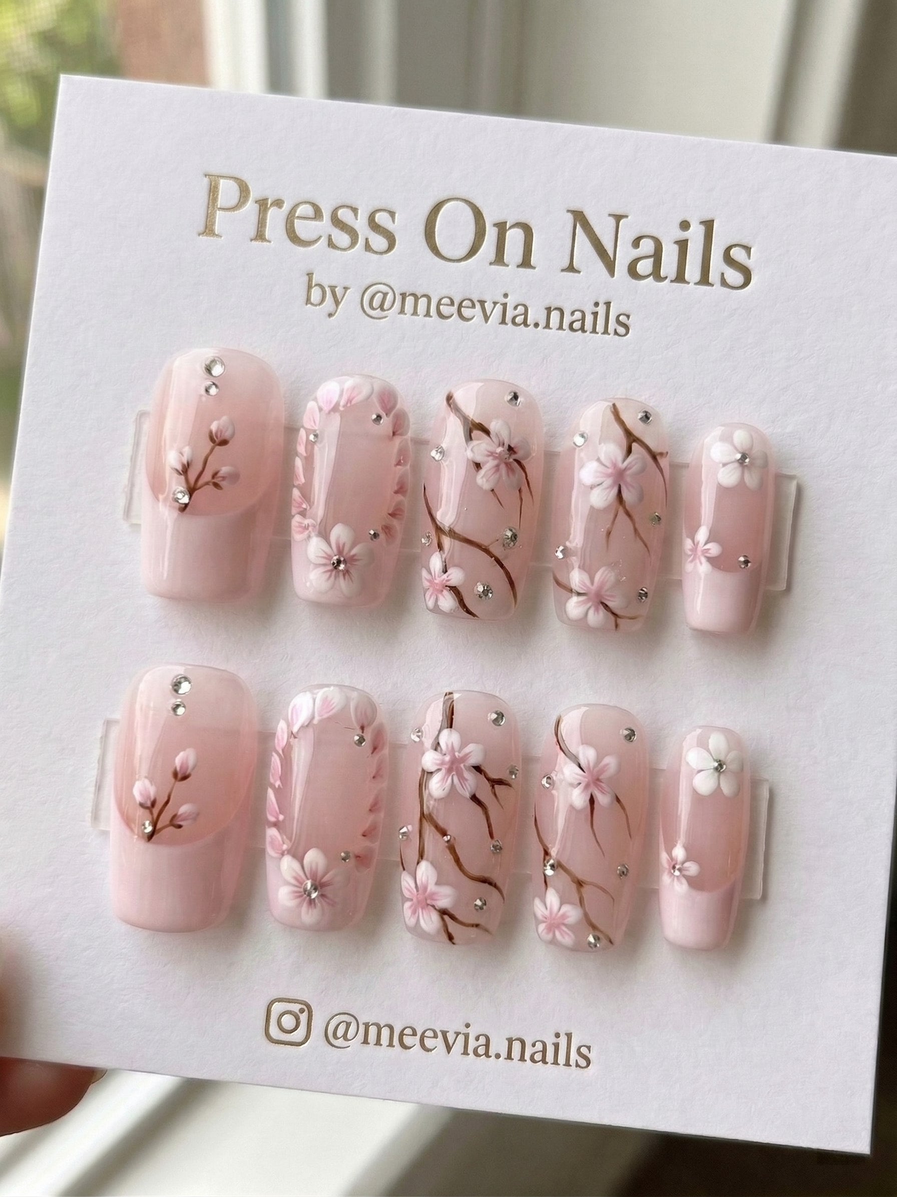 Square-shaped pink press-on nails with cherry blossom floral art and small rhinestones
