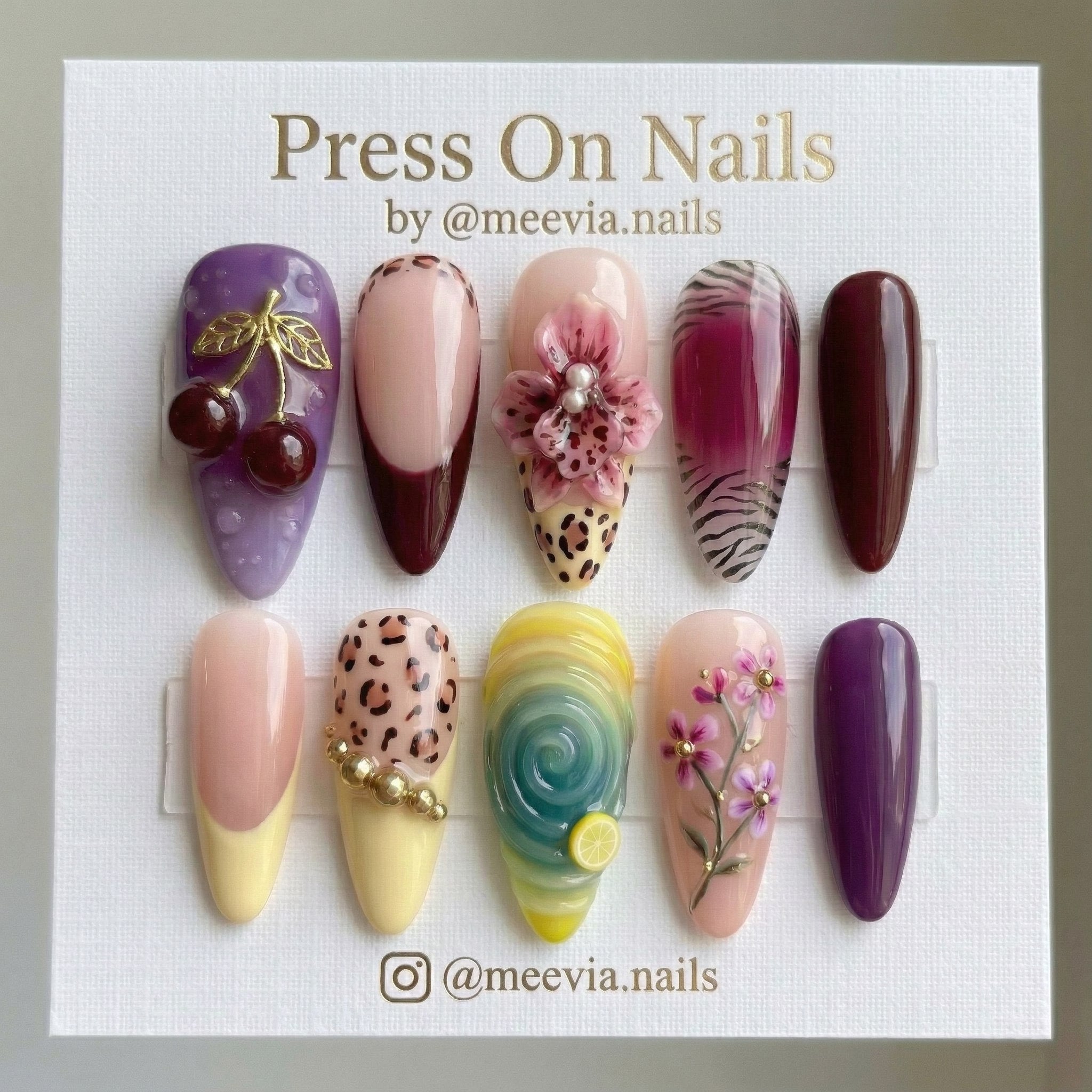 Stiletto press-on nail set featuring 3D cherries, leopard print, and floral designs in purple and burgundy.