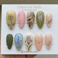 Long almond-shaped botanical garden press-on nails with mixed floral art and crystal embellishments.