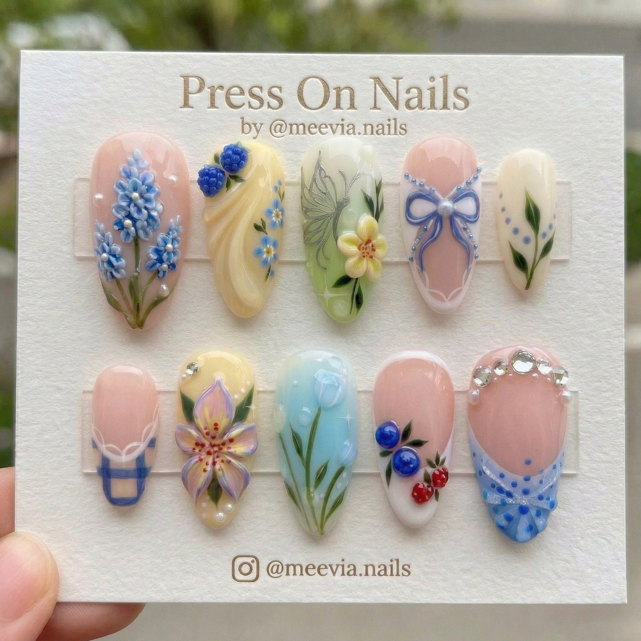 Almond-shaped pastel press-on nail set with 3D berries, blue bow, and floral nail art designs.