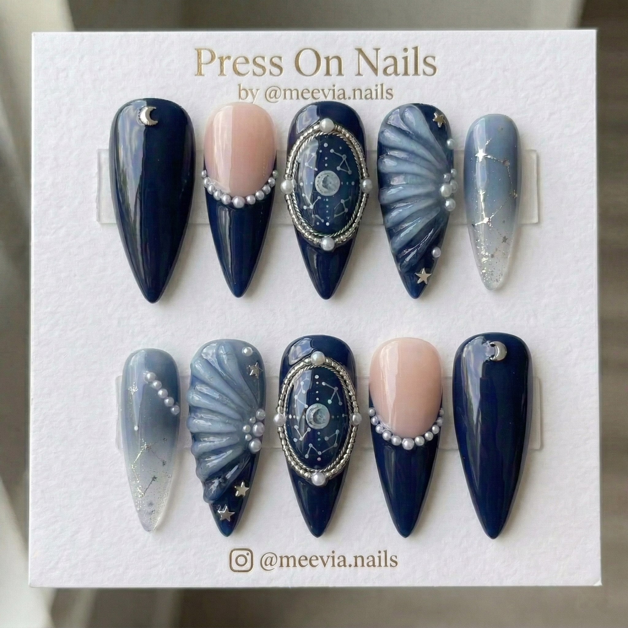 Stiletto-shaped navy blue celestial press on nails with pearls, stars, and 3D shell textures
