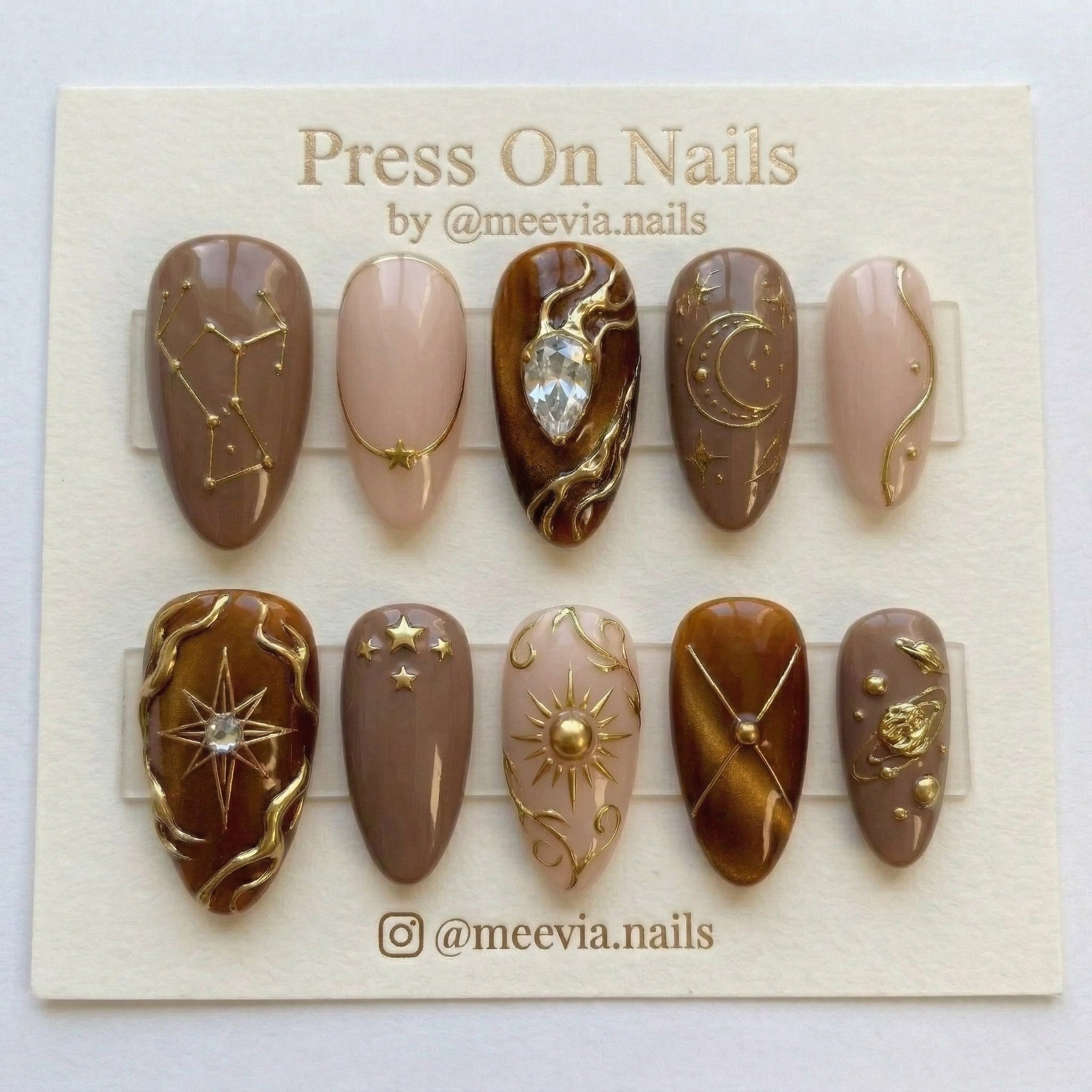 Almond-shaped brown celestial press-on nail set with gold 3D sun, moon, and planet motifs