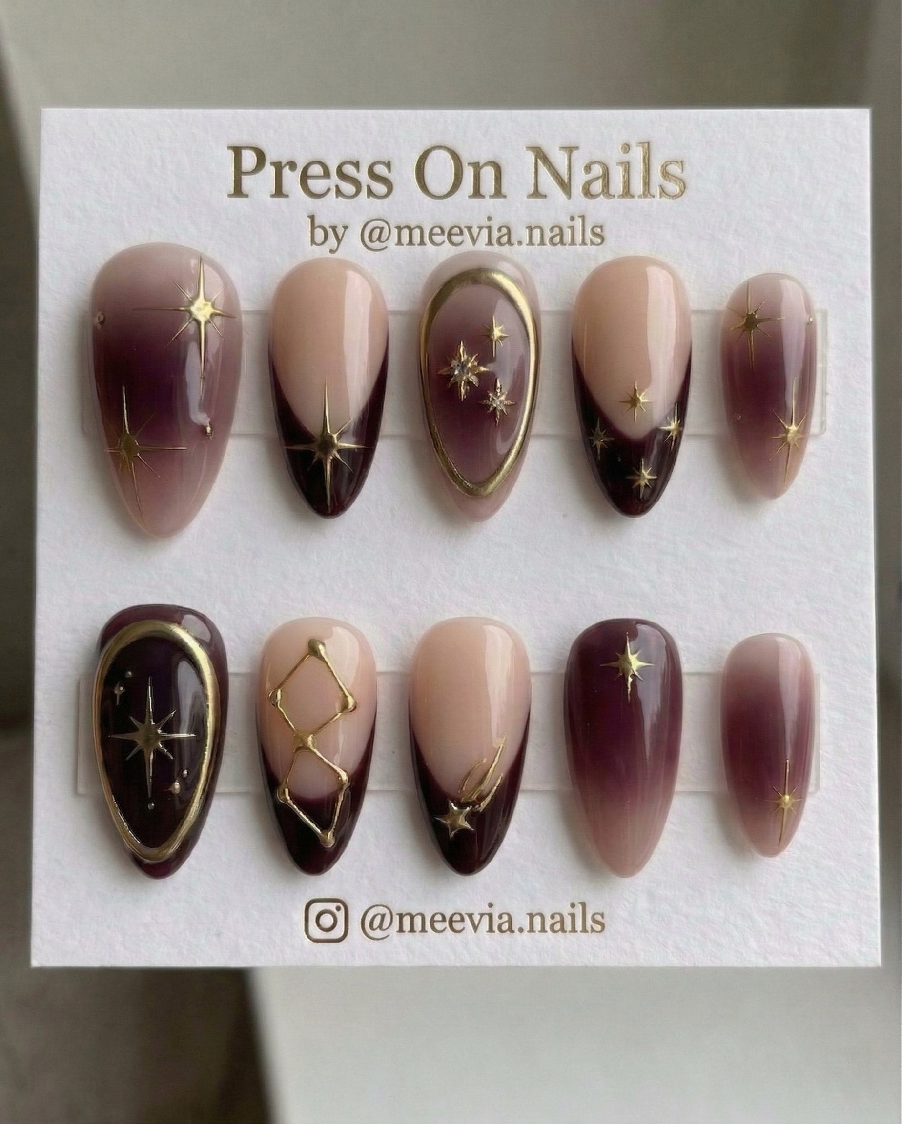Almond-shaped celestial press-on nail set with burgundy French tips and 3D gold stars