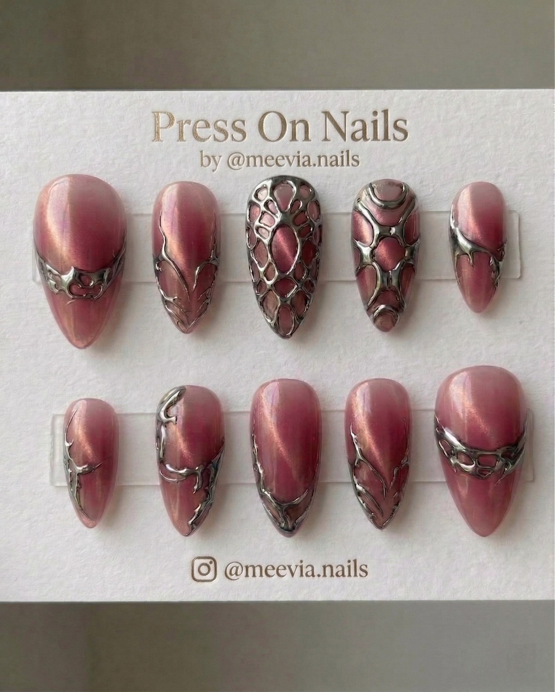 Stiletto-shaped pink cat-eye press-on nails with 3D silver chrome web patterns