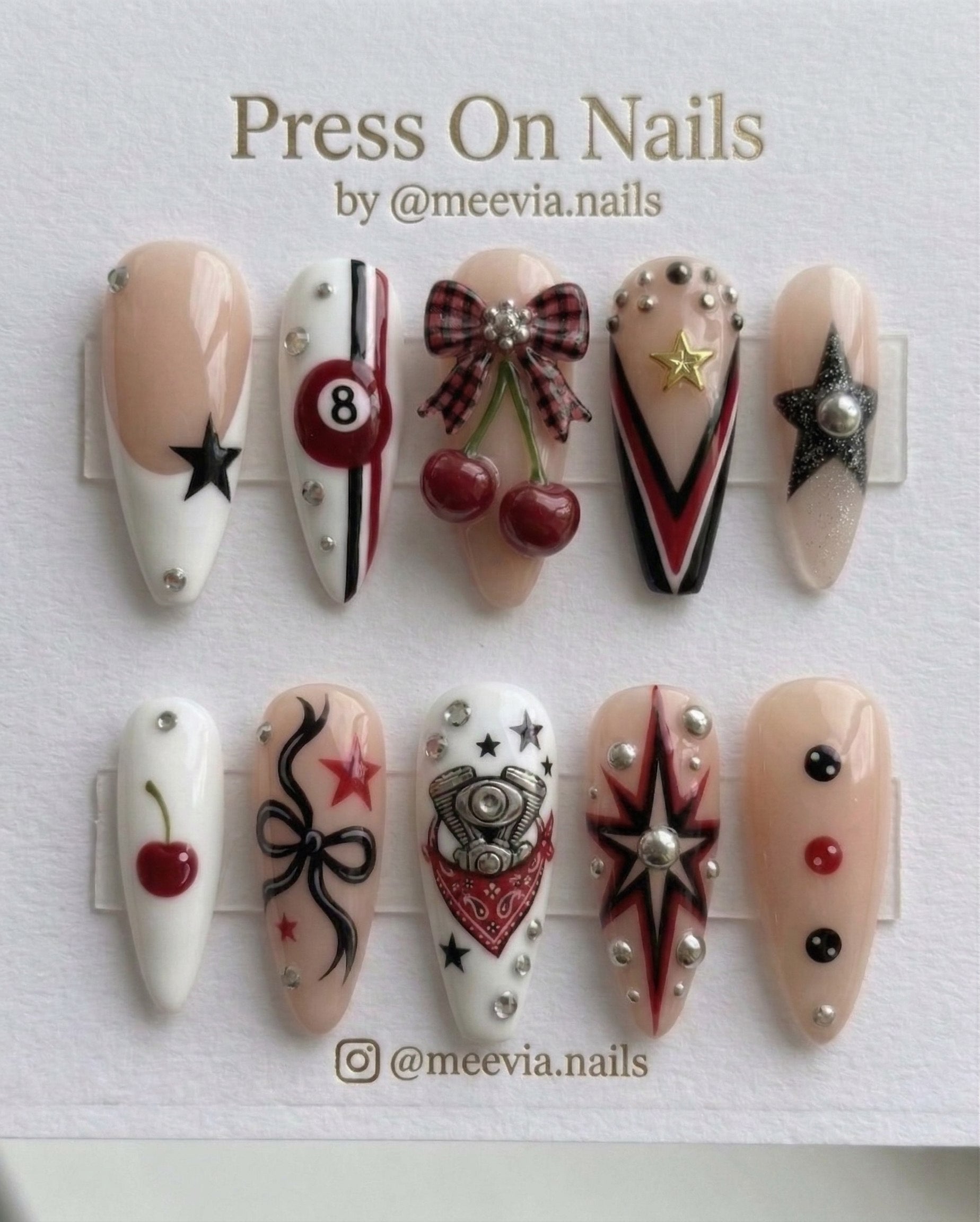 Almond-shaped press on nails featuring 8-ball, cherry, and bow 3D nail art in red, black, and white.