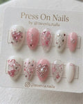 Almond-shaped white and pink press on nails with 3D hearts, silver chains, and bows.
