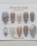 Almond-shaped press-on nails with 3D floral art, pearls, and soft blue gradients.