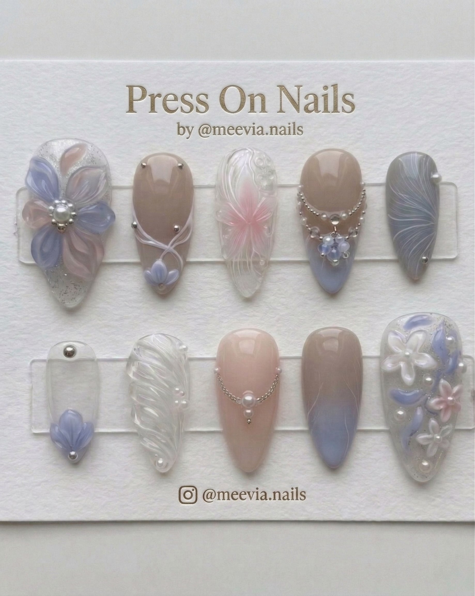 Almond-shaped press-on nails with 3D floral art, pearls, and soft blue gradients.