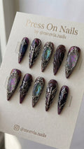 Stiletto-shaped purple shimmer press-on nails with 3D silver gothic designs and iridescent abalone shell inlays