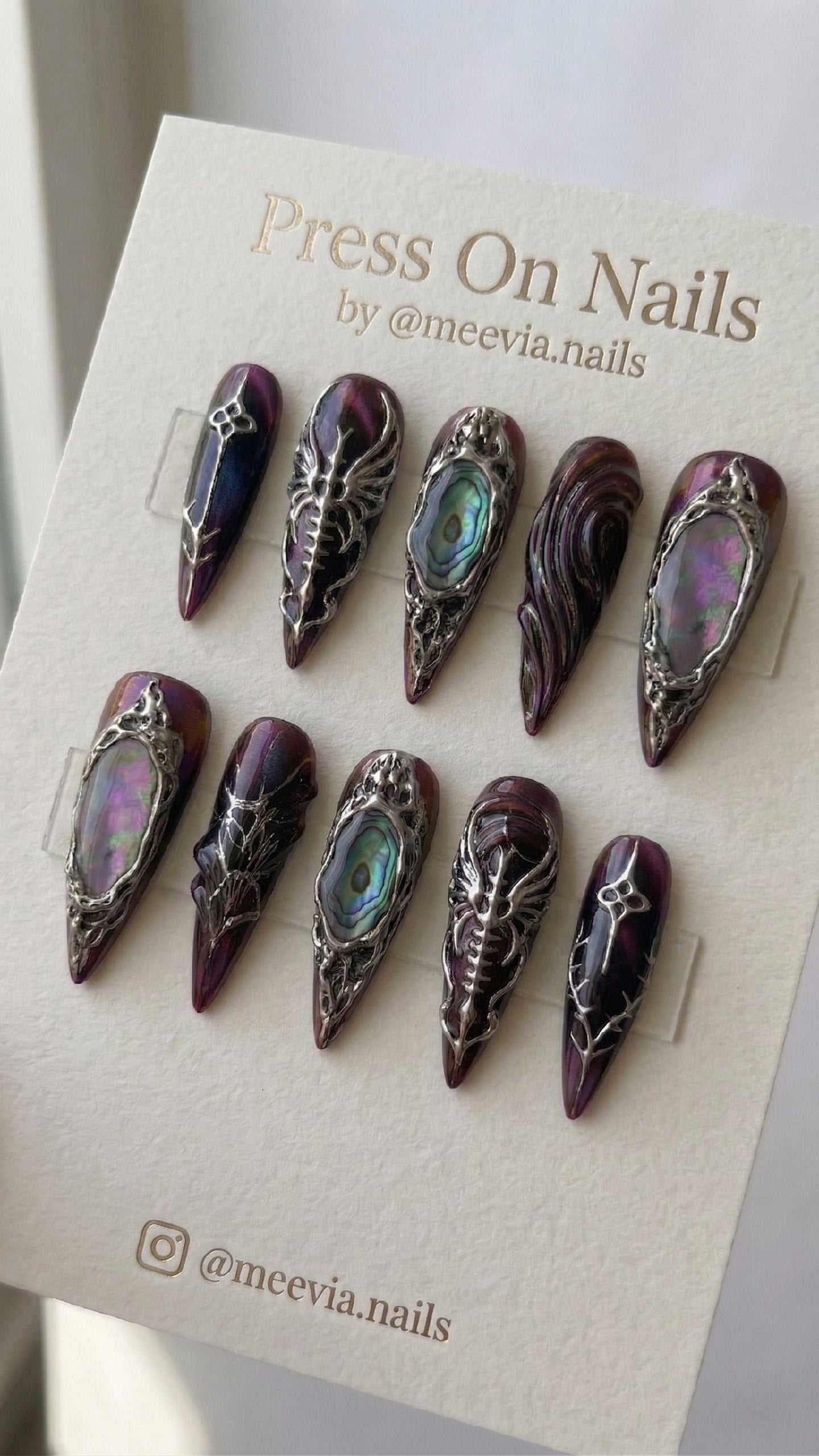 Stiletto-shaped purple shimmer press-on nails with 3D silver gothic designs and iridescent abalone shell inlays