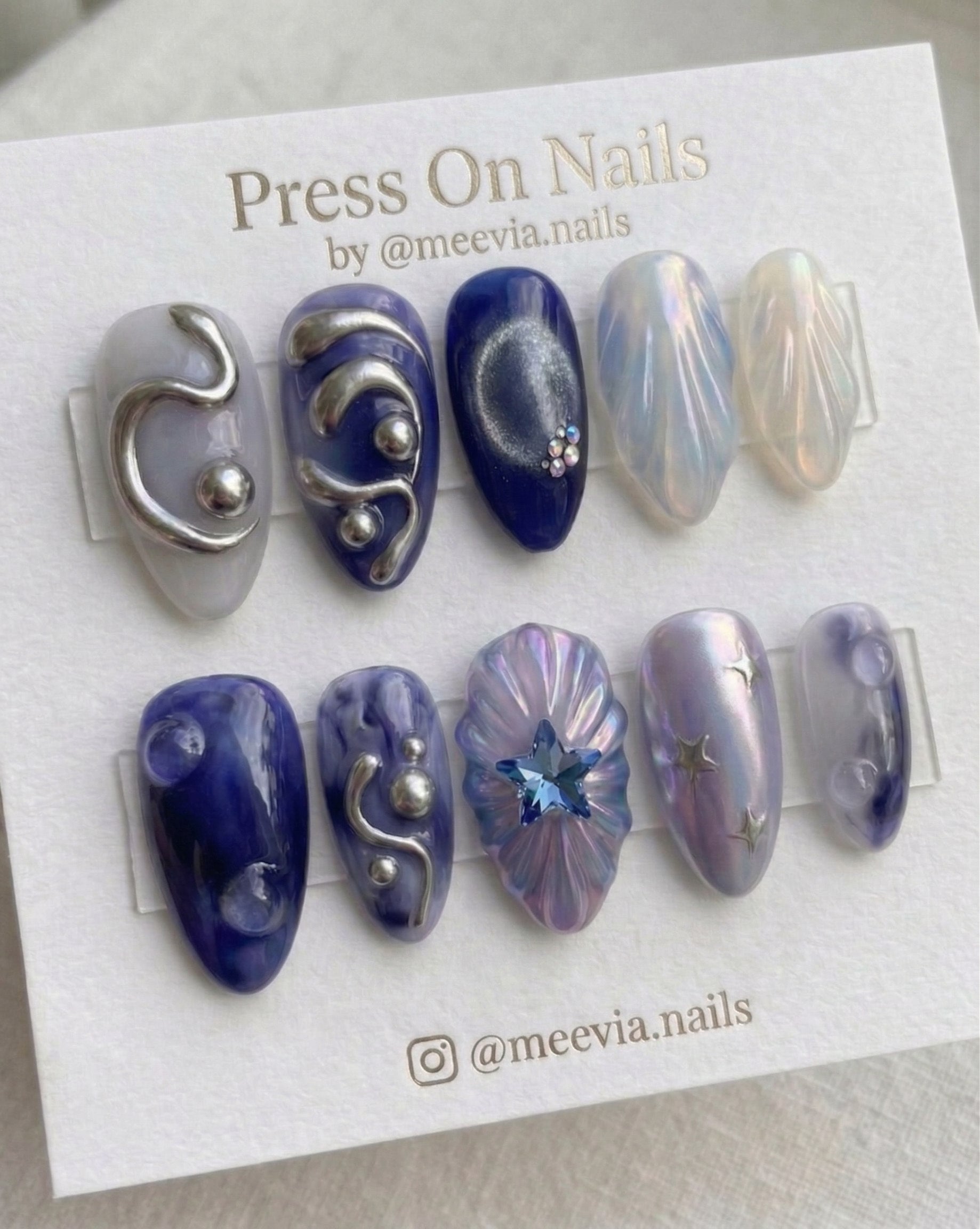 Almond-shaped celestial press-on nails with 3D silver swirls, blue star gem, and galaxy patterns.