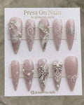Long stiletto press-on nails with pink shimmer, 3D silver bows, and white snowflake nail art.