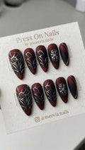 Stiletto-shaped red and black matte press-on nails with 3D silver metallic gothic designs