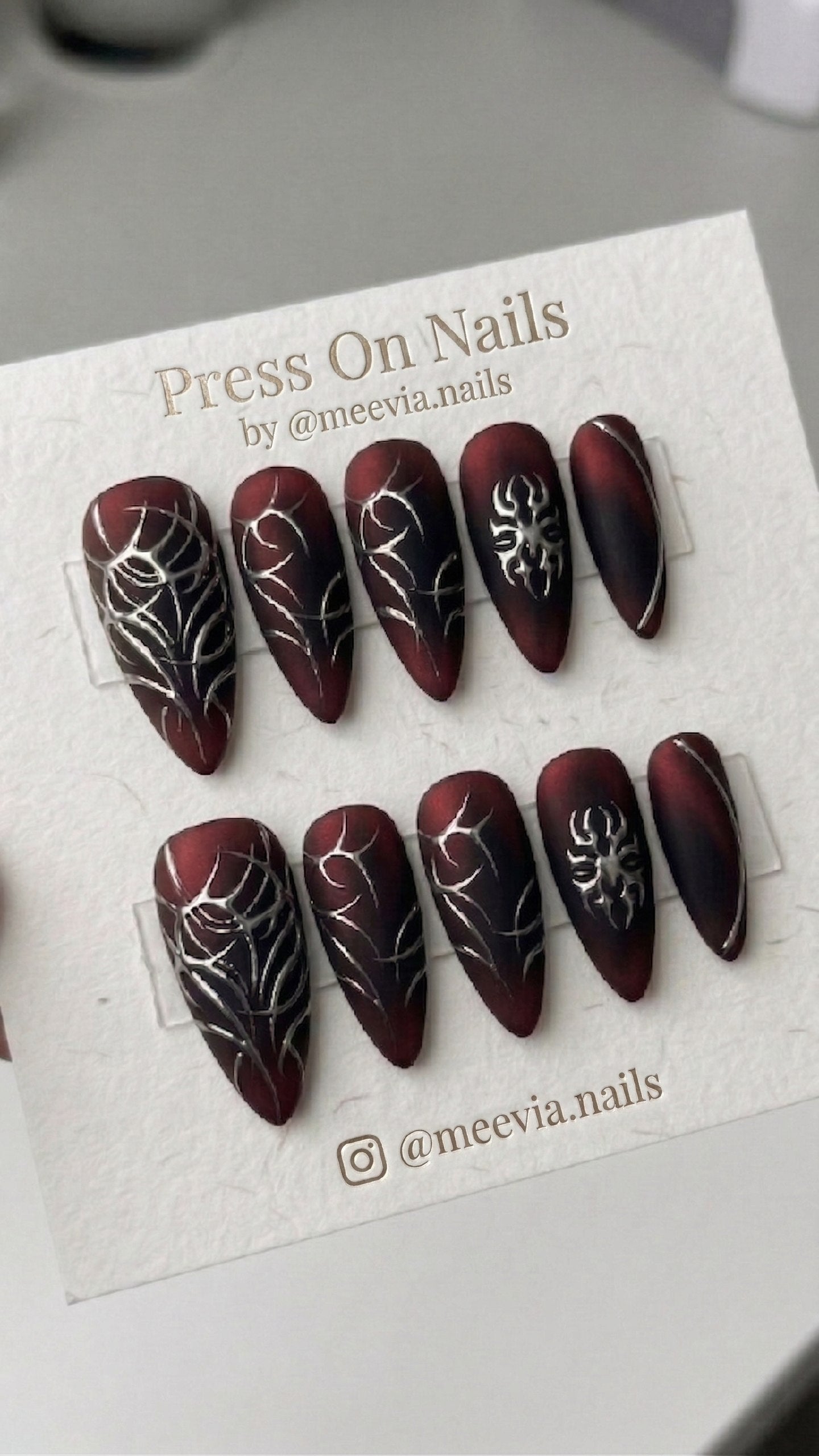 Stiletto-shaped red and black matte press-on nails with 3D silver metallic gothic designs