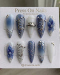 Stiletto-shaped blue and white press-on nails with 3D butterfly wings and chrome nail art.