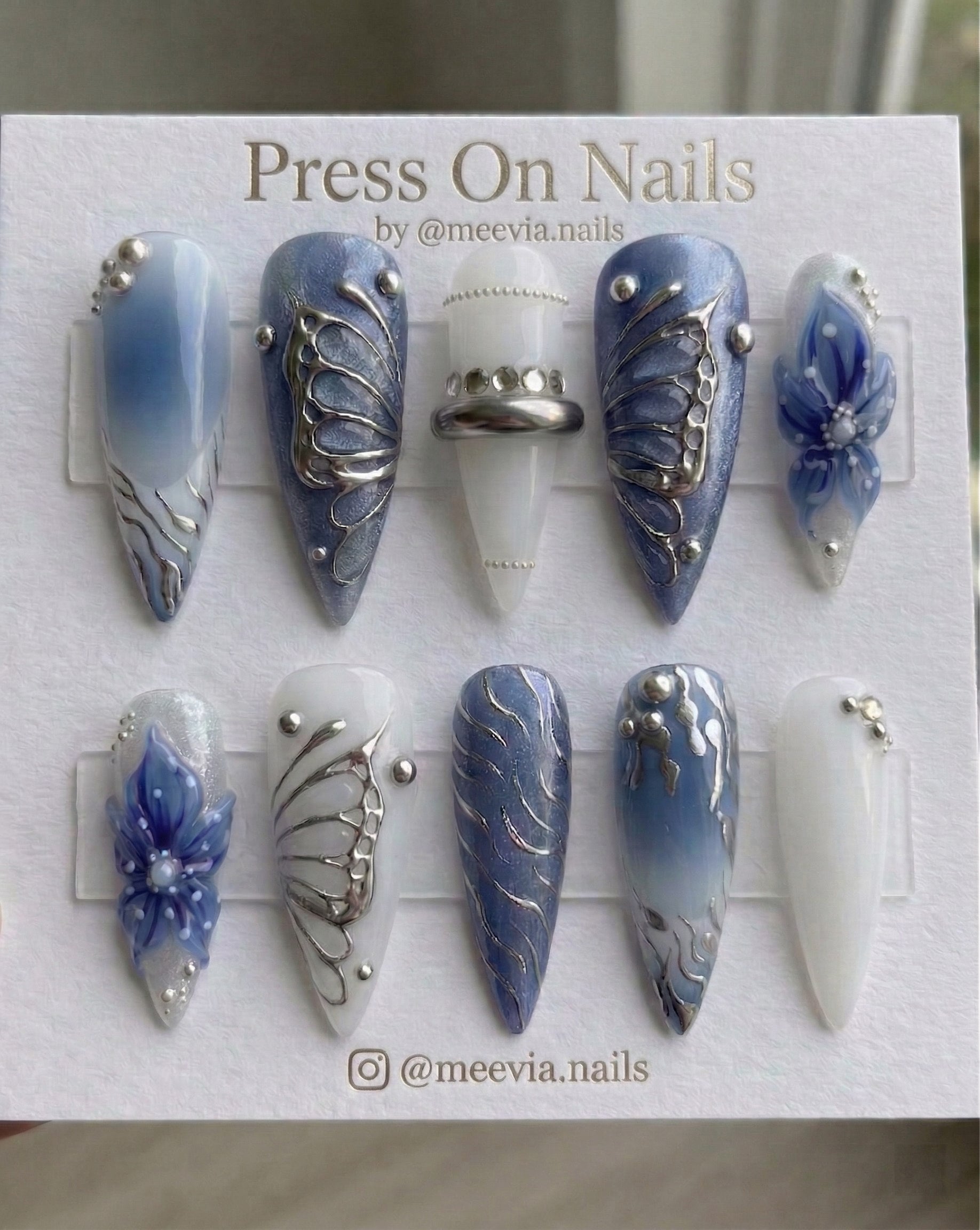 Stiletto-shaped blue and white press-on nails with 3D butterfly wings and chrome nail art.