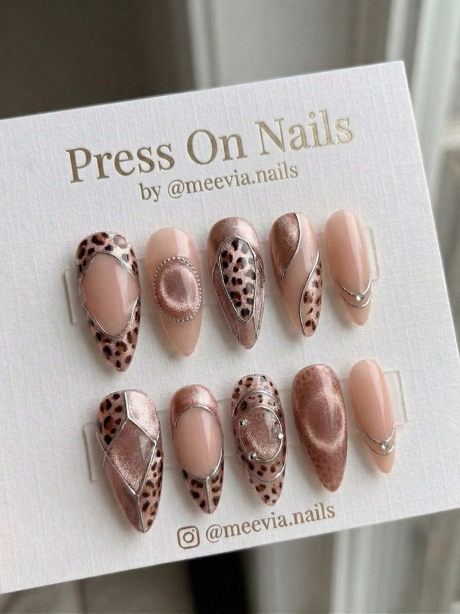 Almond-shaped rose gold press-on nails with leopard print and silver chrome 3D outlines.