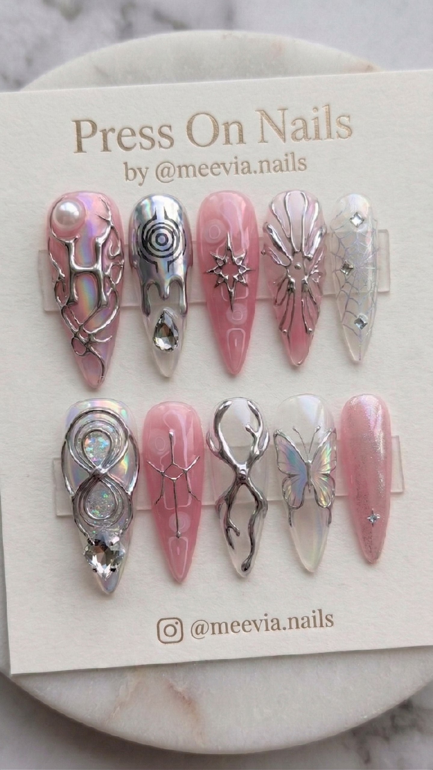 Stiletto-shaped pink press-on nail set with 3D silver metallic art, iridescent finishes, and crystal embellishments.