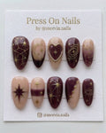 Almond-shaped burgundy and nude press-on nail set with gold celestial stars and galaxy motifs