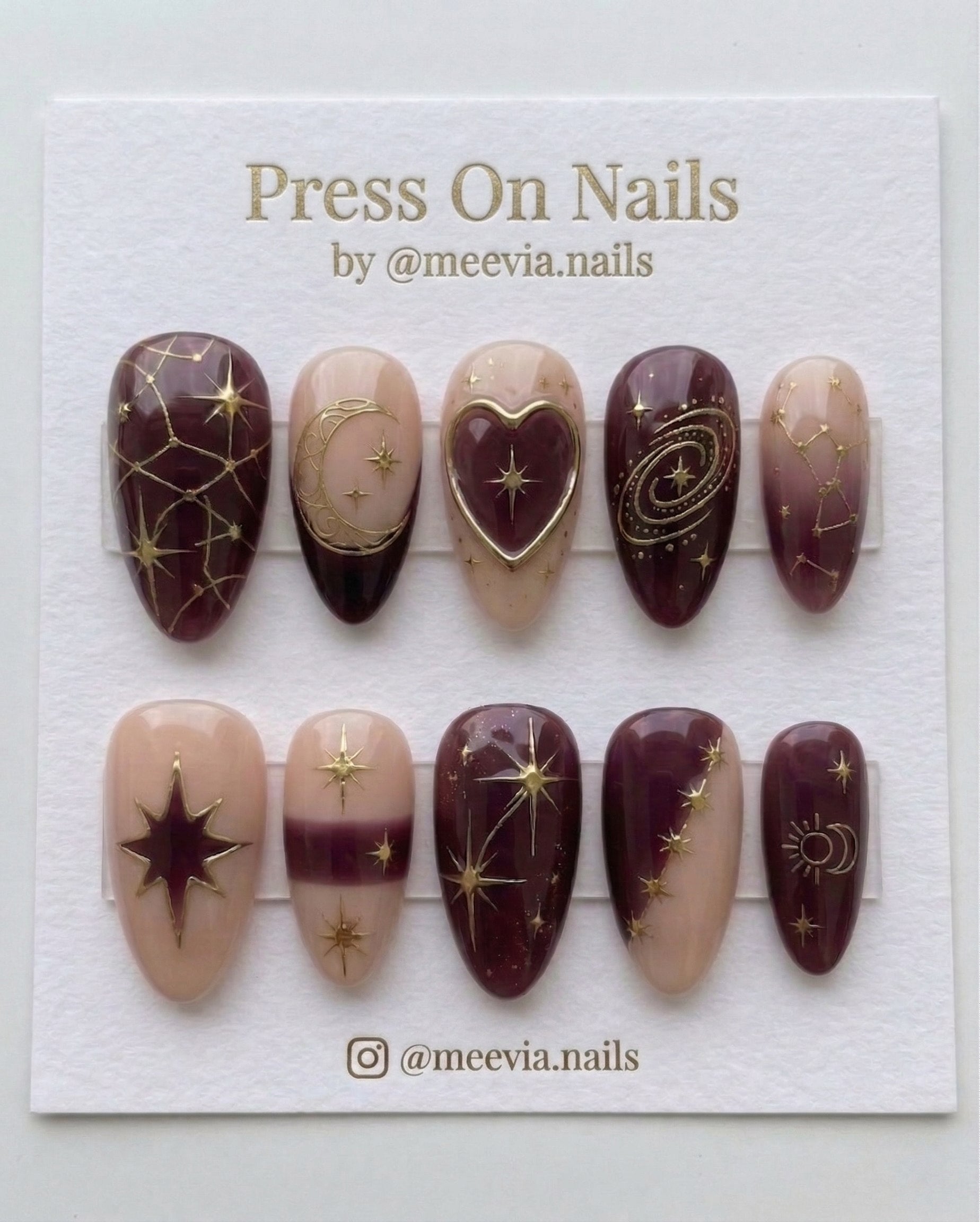 Almond-shaped burgundy and nude press-on nail set with gold celestial stars and galaxy motifs