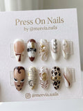 Stiletto-shaped eclectic press-on nails with mixed media designs including leopard print and 3D gold charms