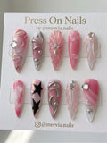Long stiletto pink marble press-on nails with silver chrome 3D waves and black star motifs.