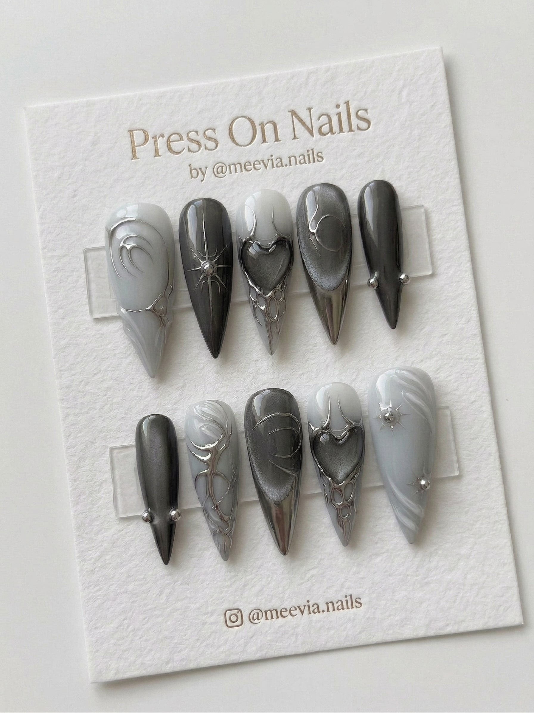 Stiletto-shaped grey and silver press-on nails with 3D chrome heart and starburst nail art