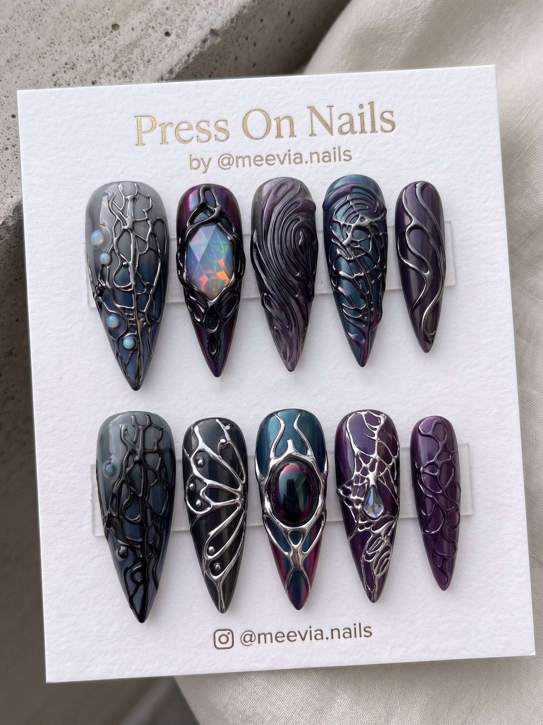 Almond-shaped mismatched press on nails featuring 3D flowers, a gold bow, and artistic character illustrations.