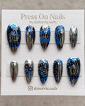 Almond-shaped iridescent chrome press-on nails with 3D silver thorns, hearts, and blue butterflies