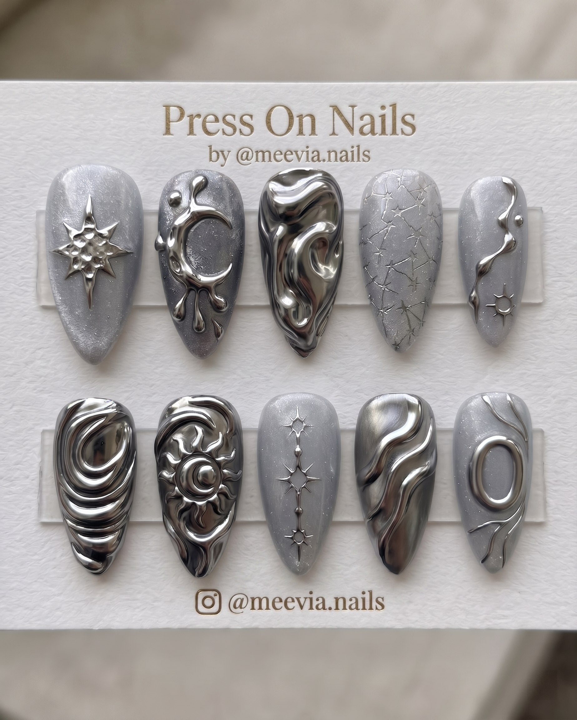 Long stiletto press-on nail set with grey cat-eye shimmer, 3D silver chrome stars, and metallic heart motifs.