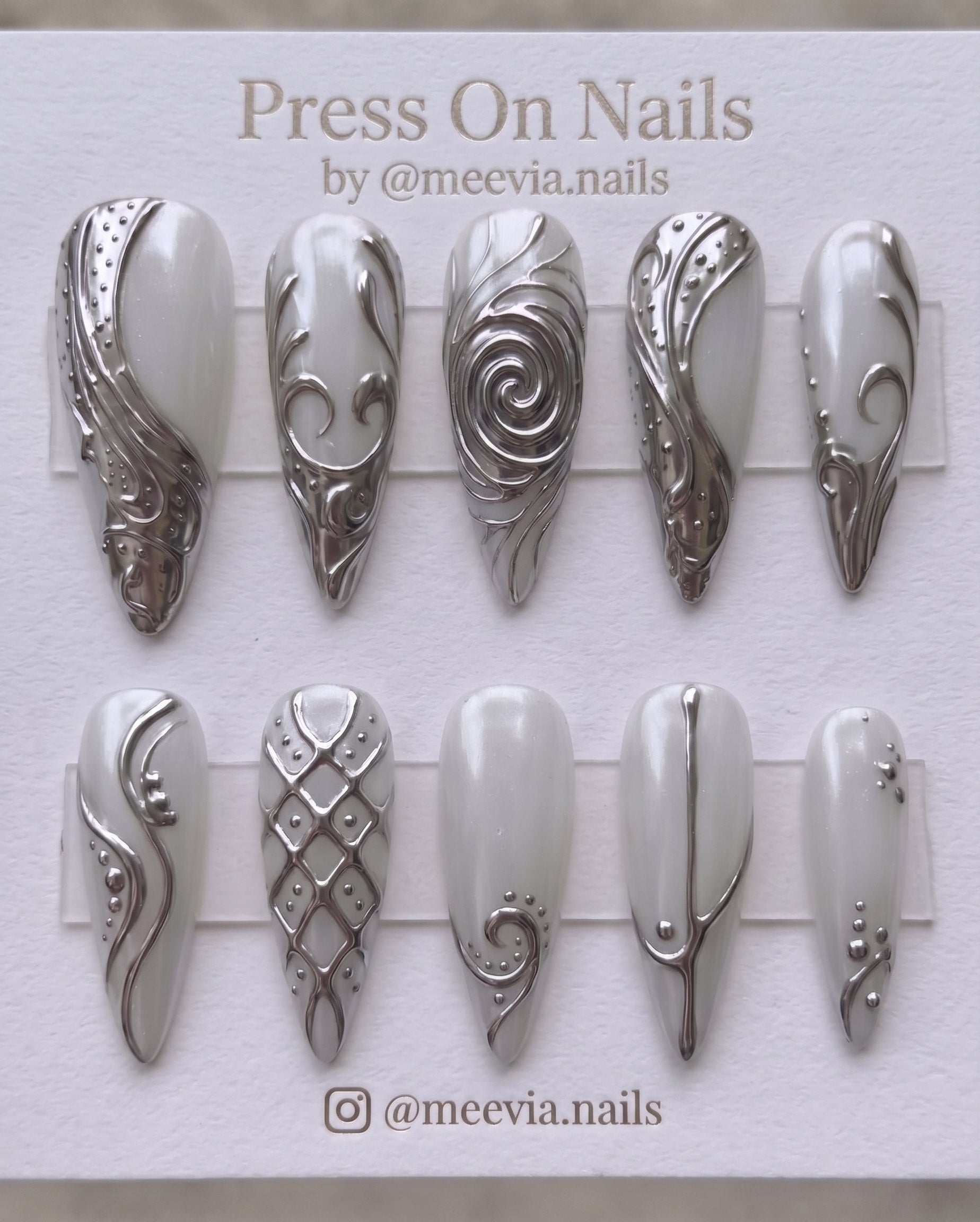 Stiletto-shaped milky white press on nails with 3D silver chrome swirls and metallic nail art