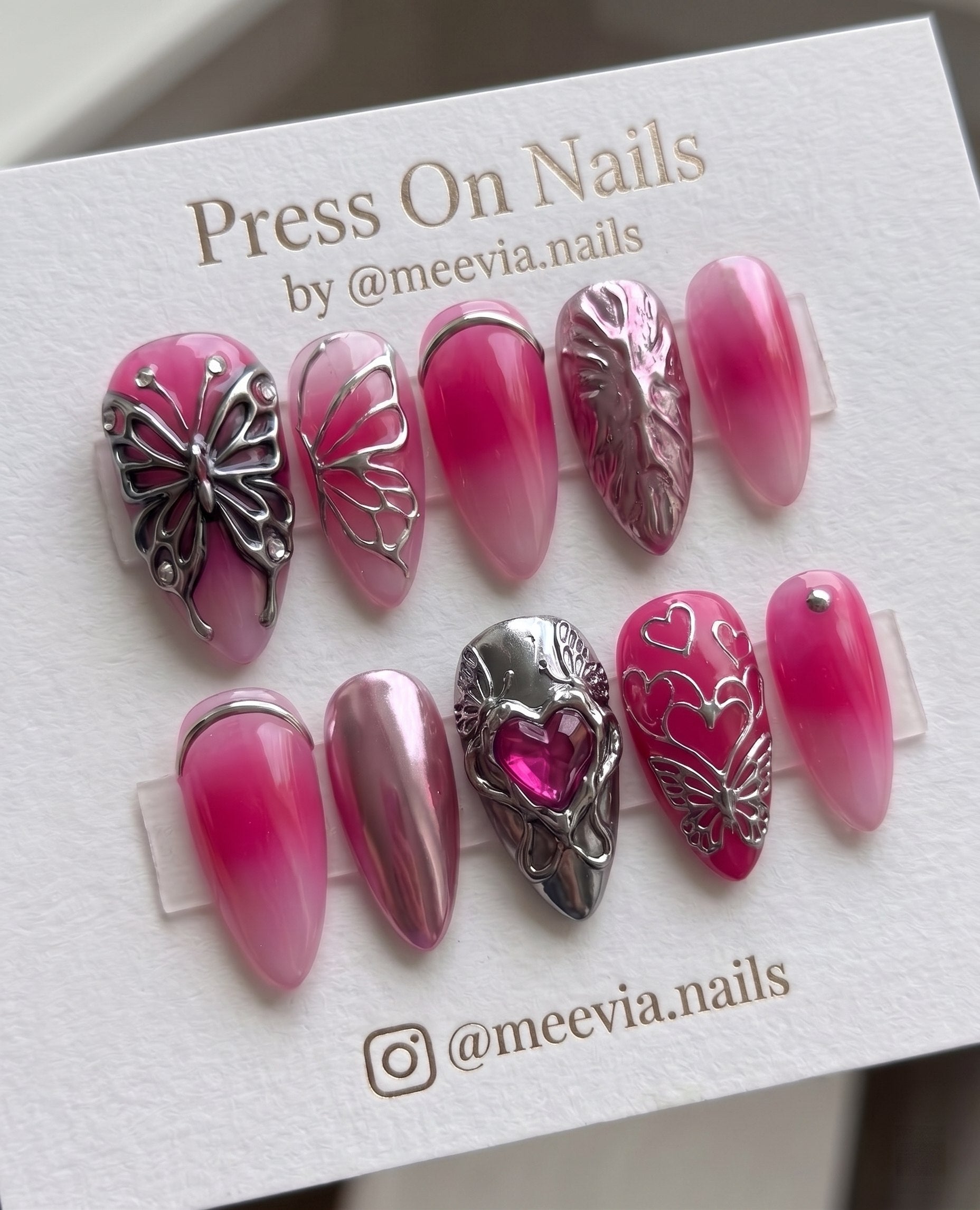 Almond-shaped pink ombre press-on nails with 3D silver butterflies and heart accents