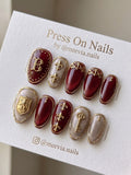 Oval-shaped burgundy and champagne press-on nail set with 3D gold royal motifs and cat-eye finish