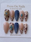 Almond-shaped western press-on nails featuring brown cow print, turquoise charms, and matte navy blue with 3D droplets.