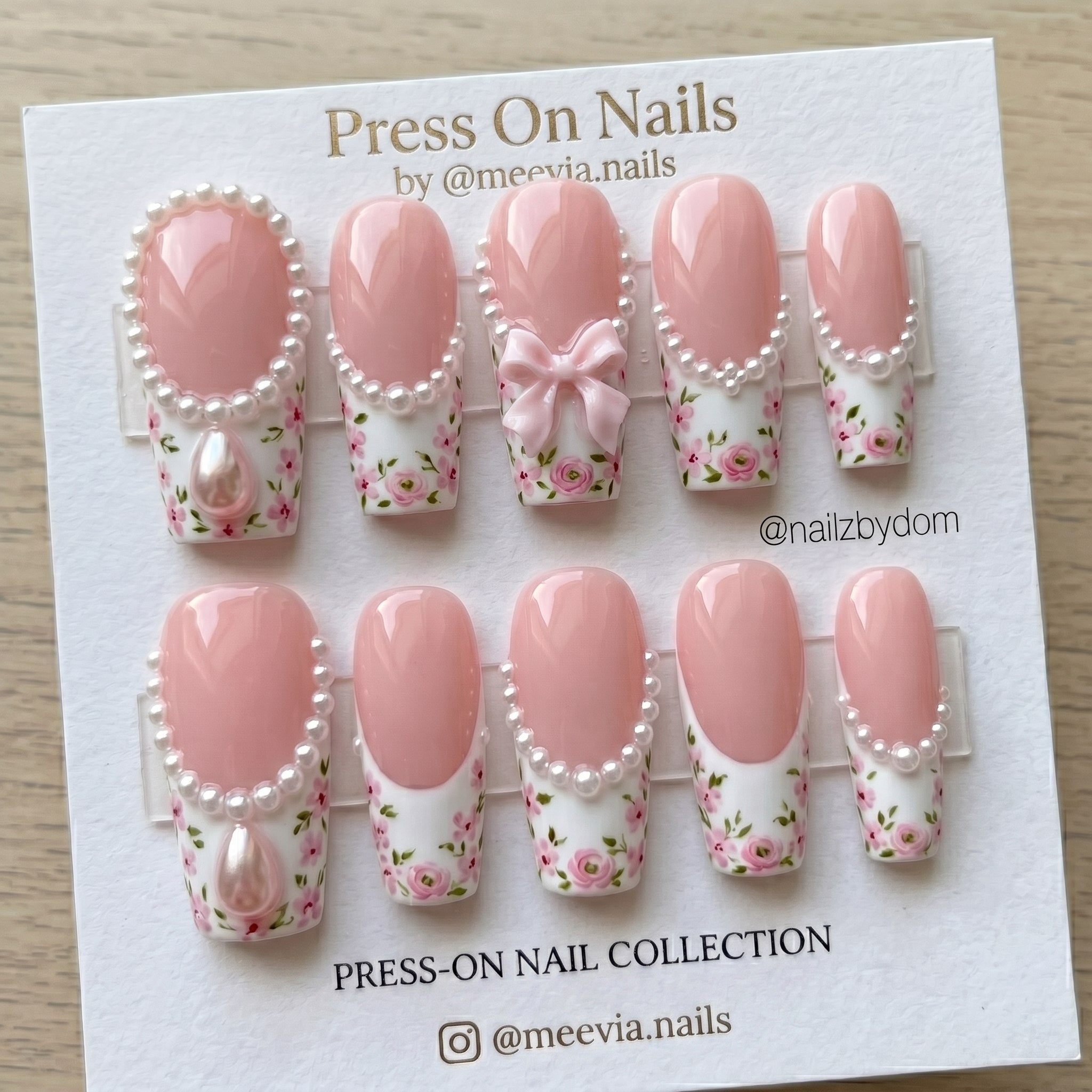 Long coffin-shaped press-on nails with pink and white floral patterns, 3D pearls, and a pink bow.