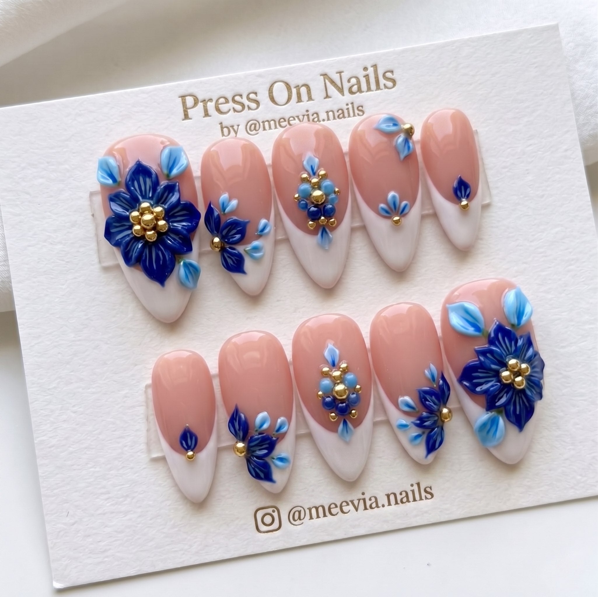 Almond-shaped French tip press-on nails with 3D blue flowers and gold accents