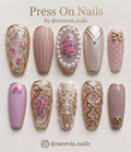 Coffin-shaped pink press-on nails with floral rose designs, gold bows, and 3D pearl embellishments.