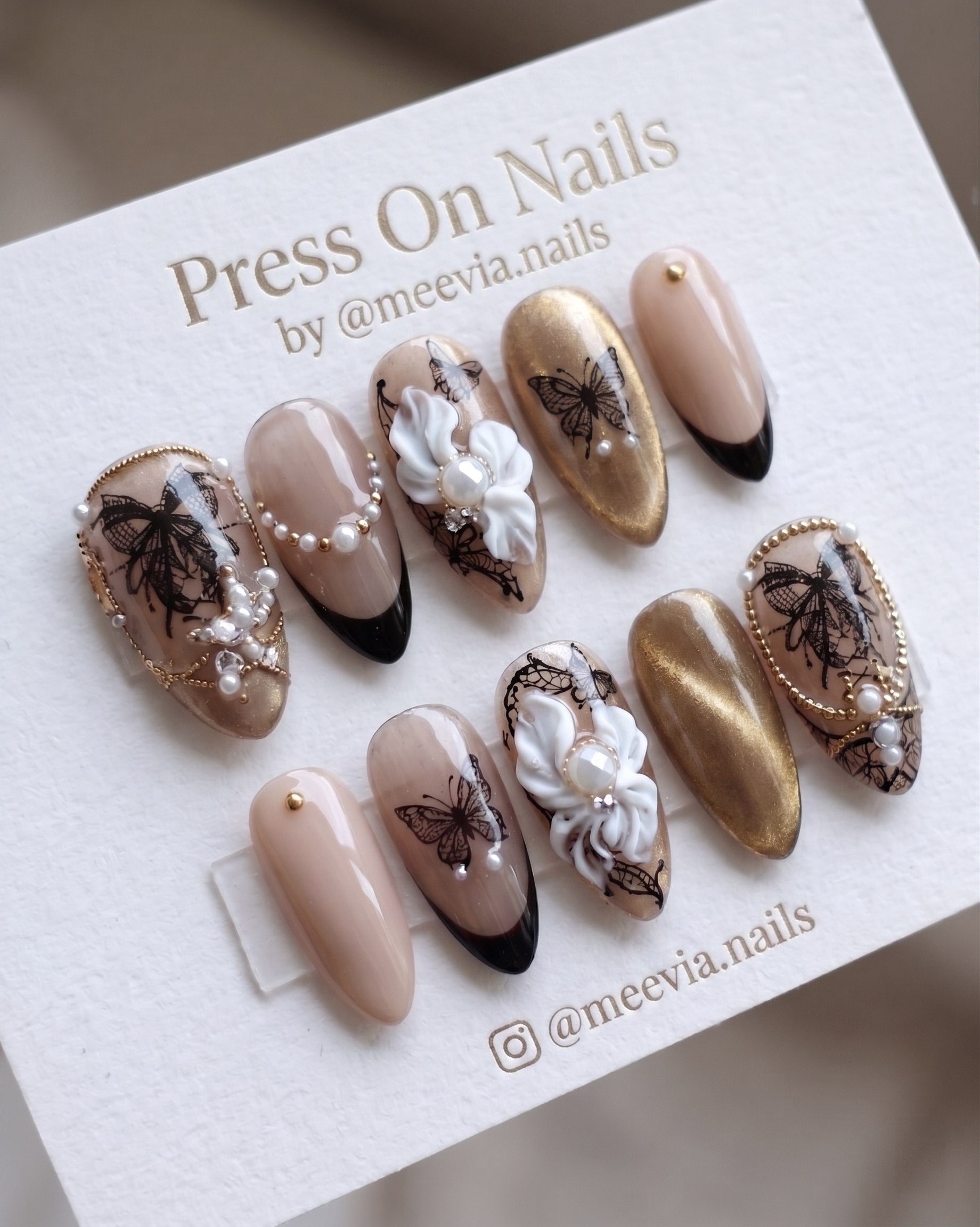 Almond-shaped nude and gold press-on nail set with 3D white flowers and butterfly motifs
