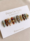 Stiletto-shaped press on nail set with tortoise shell patterns, sage green tones, and raw stone 3D nail art.