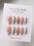 Almond-shaped pink press on nails with polka dots, pearls, and gold chain accents.