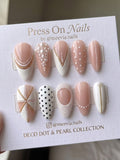Almond-shaped nude and white press on nails with pearls and gold dot accents.
