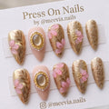 Stiletto-shaped gold embossed floral press-on nails with 3D pink flowers and pearl accents.