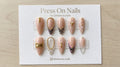 Stiletto-shaped nude press-on nails featuring zebra print, gold chains, and 3D stud nail art details.