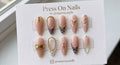 Stiletto-shaped nude press-on nails with black zebra print, gold chain embellishments, and white geometric lines.