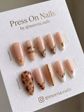 Almond-shaped nude press-on nails with gold bead chain charms and marble accents