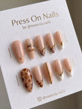 Almond-shaped nude press-on nails with gold bead chains and marble accents.