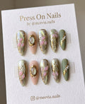 Stiletto-shaped sage and nude press-on nails with 3D gold frames, pearls, and gold leaf accents