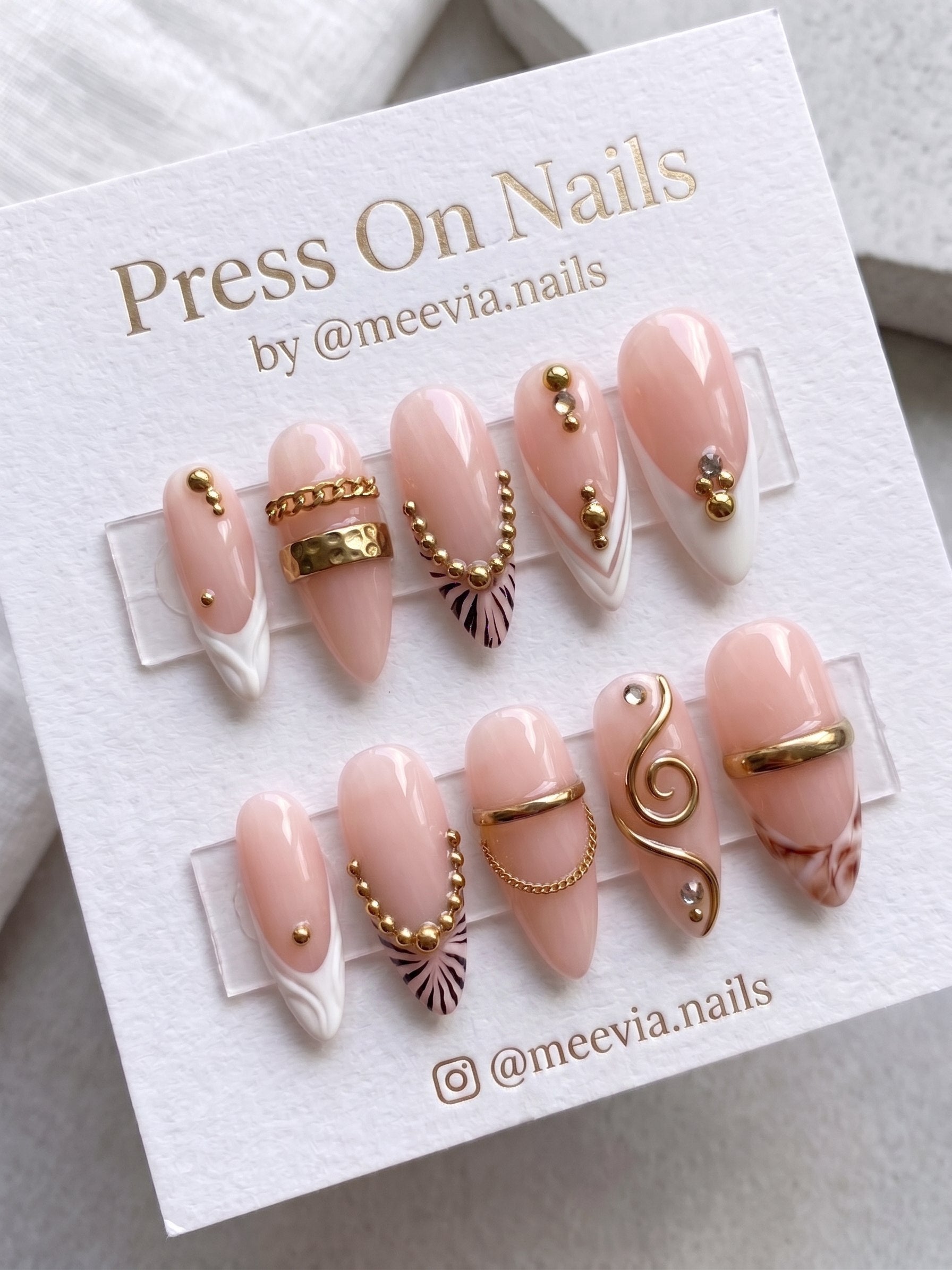 Almond-shaped nude press-on nails with gold 3D accents and white French tips